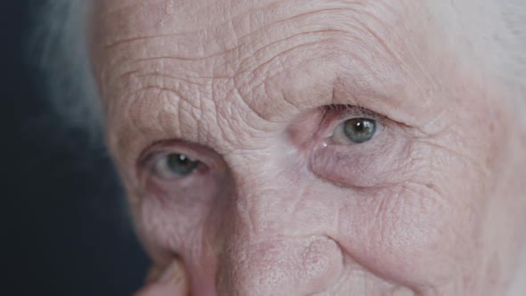 Close Look Into Camera of Wrinkled Cute Grandmother on Background