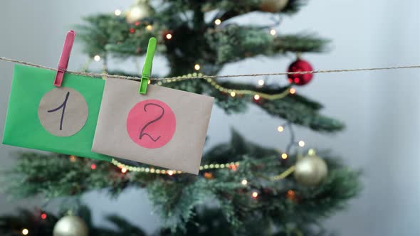 Woman Hangs Up Homemade Christmas Advent Calendar Multicolored Envelopes with Numbers Against the