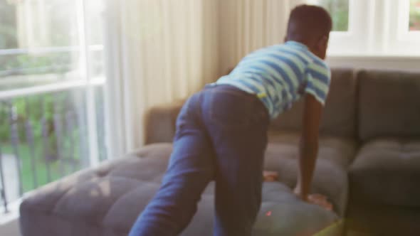 Smiling african american boy jumping on the couch at home