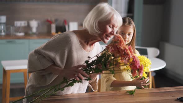 Cheerful girl helps to grandmother collect bouquet of flowers