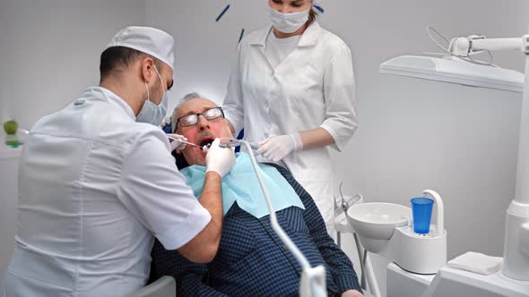 Male Stomatologist Working with Aged Patient Treating Teeth Using Equipment