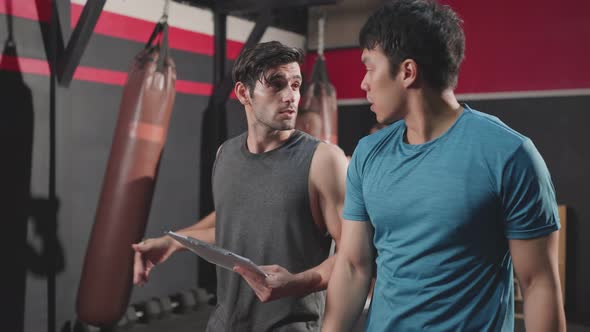 Caucasian male trainer take sportsman walking around gym to create fitness training program.