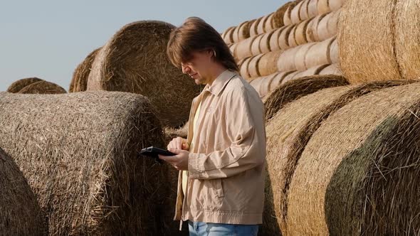 Farmer Agronomist Checks Hay Bales on the Wheat Field After Harvest at Sunset