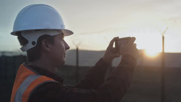 A Male Engineer Takes a Photo of a Plantation or Solar Panel Plant on a Smartphone