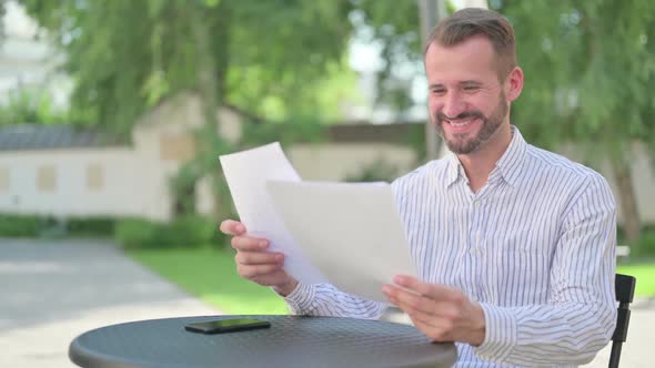 Middle Aged Man Celebrating Success While Reading Documents