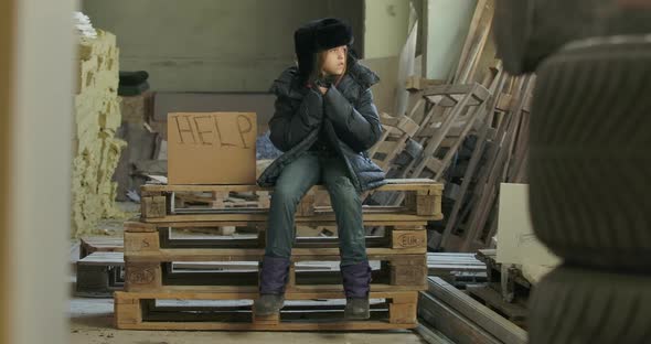 Little Ukrainian Refugee in Dirty Warm Clothes Sitting on Pallets at the Construction Site with Help