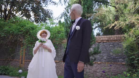 Excited Groom with Grey Hair Admiring Happy Bride Standing at Background Turning Gesturing Success