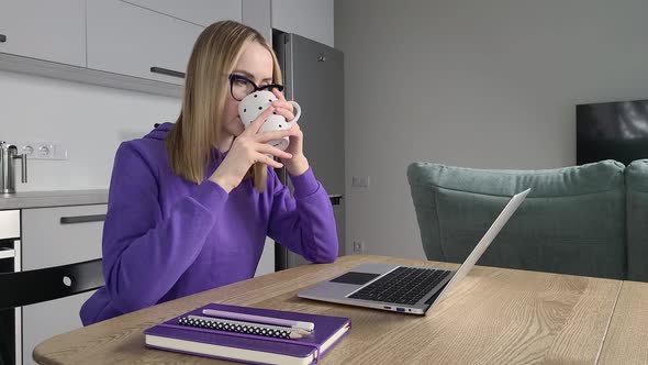 Pensive Young Adult Woman in Glasses Work Study at Kitchen Using Laptop