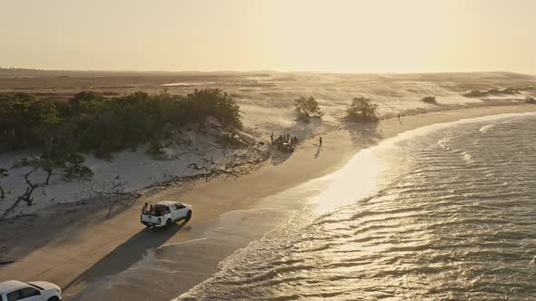 Kite surfers on pickup trucks arriving at Guriu beach in warm sunset glow; drone