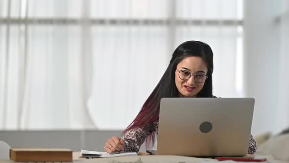 Asian woman sits in office and communicates with client on  video call on laptop