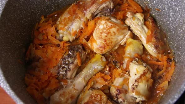 Fresh chicken pieces in the frying pan with onion and carrot close up