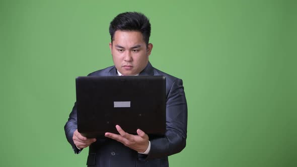 Young Handsome Overweight Asian Businessman Against Green Background