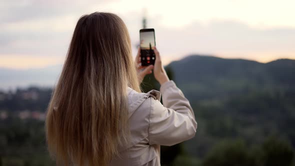 Blonde Woman Takes a Photo of Mountains with a Smartphone in Her Hands