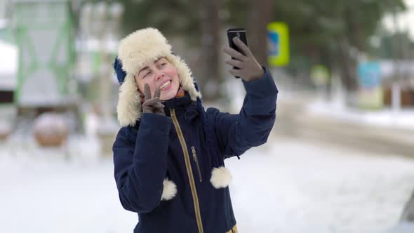 Smiling woman in a hat with earflaps and a jacket, who takes a selfie on her smartphone