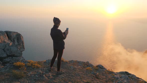 Circular Shot From the Back of a Girl Standing on the Edge of a Cliff Who Takes Video and Pictures