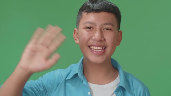The Happy Young Asian Boy Waving Hand And Say Bye Bye While Standing On Green Screen In The Studio