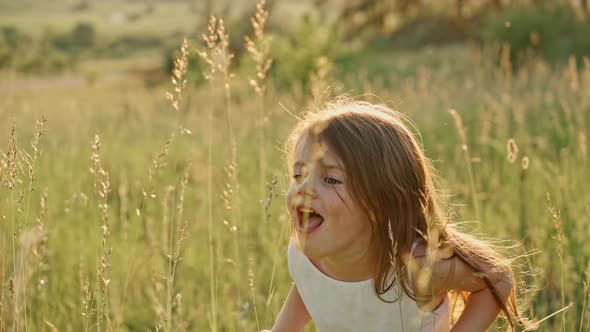 Portrait of a Cute Girl with Flowing Hair in a White Summer Dress Standing on a Green Lawn Smiling