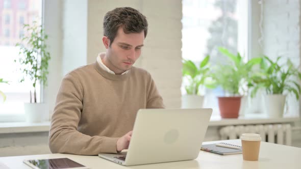 Man Looking at Camera While Using Laptop in Office