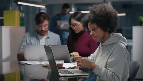 AfricanAmerican Female Entrepreneur Work on Laptop and Chat on Smartphone in Office