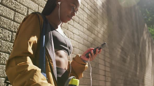 African american woman exercising outdoors wearing earphones using smartphone in the city