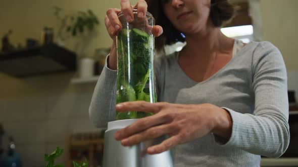 Caucasian woman preparing green vegetable smoothie in kitchen