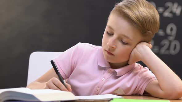 Bored School Boy Writing Notes in Copy Book on Lessons, Uninteresting Subject