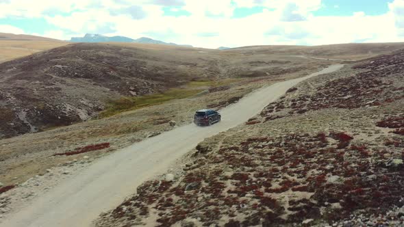 Aerial drone of a red suv driving along a dirt road path in the high-altitude alpine plain and mount