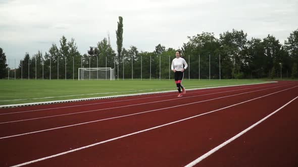 Young woman is running in the stadium. woman with white sweater and black tights. Camera pans to lef