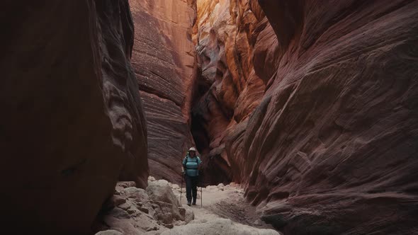 Hiker Walking On Dry Curve Riverbed In Deep Slot Canyon With Orange Smooth Rocks