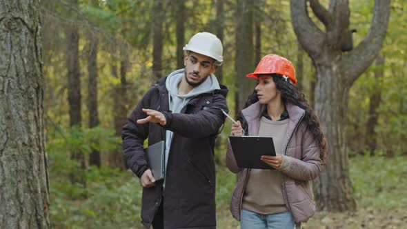 Young Diverse Employees in Helmets Indian Man and Oriental Woman Forestry Engineers in Hardhats with