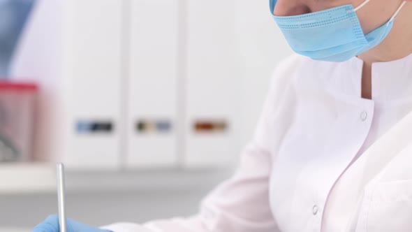 Woman Doctor Surgeon in White Uniform and Mask is Writing Diagnosis and Examination Results