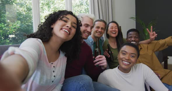 Diverse group of happy male and female friends smiling and taking selfie in living room