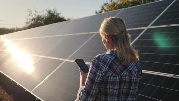 Bakc View of Woman with Smartphone Goes Aquarius Solar Panels at Home Solar Power Plant