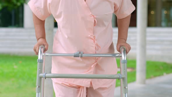 Happy old elderly Asian woman uses a walker and walks in the hospital after recovering from an accid