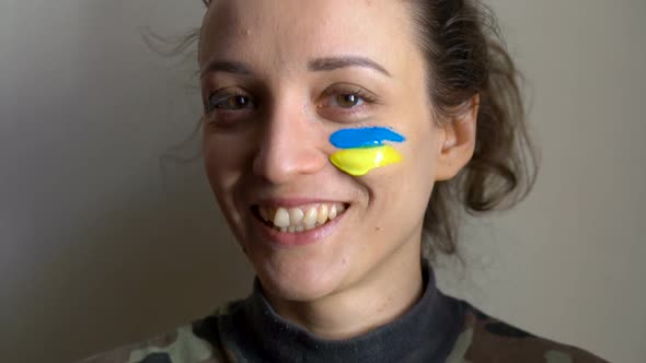 Indoor Portrait of Young Girl with Blue and Yellow Ukrainian Flag on Her Cheek Wearing Military
