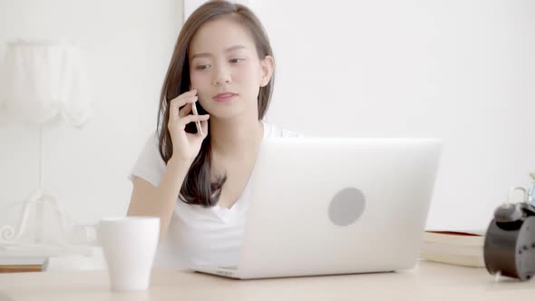 Young freelance asian woman smiling working on laptop computer and talking smart phone.