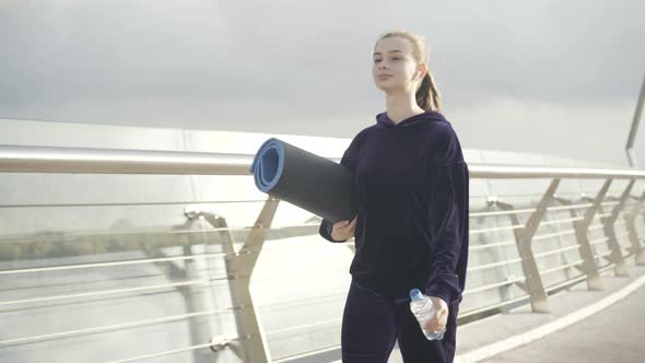 Confident Caucasian Woman Walking in Sunrays with Exercise Mat Outdoors