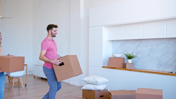 Joyful couple puts large cardboard boxes on stack on new flat floor