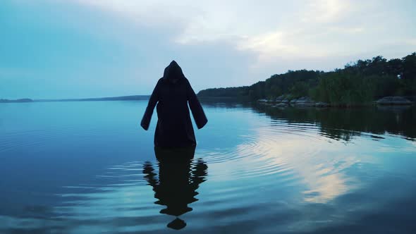 Evil witch in black cloak with hood in the river. Halloween costume.