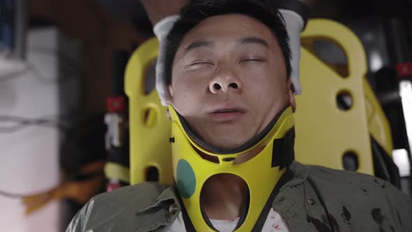 Asian Man in Neck Collar on Stretcher Riding in Ambulance