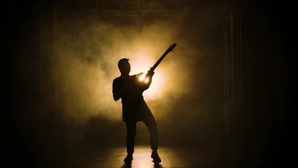 Silhouette of a Young Guy Playing on the Electric Guitar on Stage in a Dark Studio with Smoke