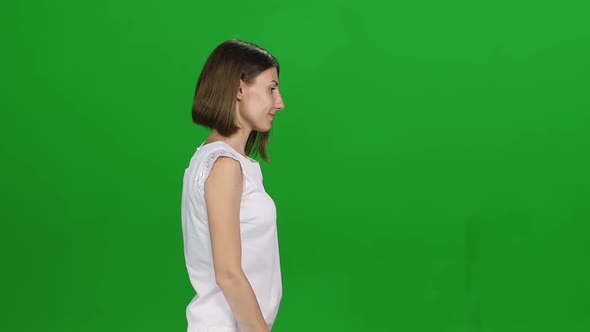 Portrait of Woman with Brown Hair and Smooth Haircut Is Calmly Walking on Green Screen. Profile View