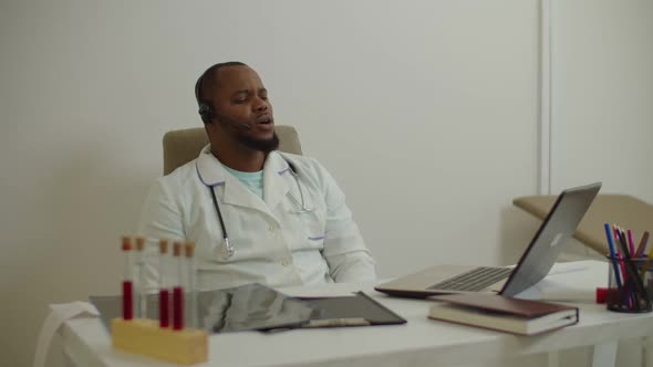 Confident African Male Doctor in Wireless Headset Consulting Patient Using Video Chat Online