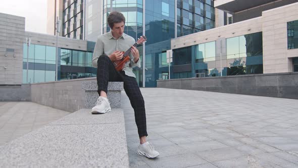 Young Adult Man Performs with Exotic Musical Instrument in Downtown on Modern Glass Office Building