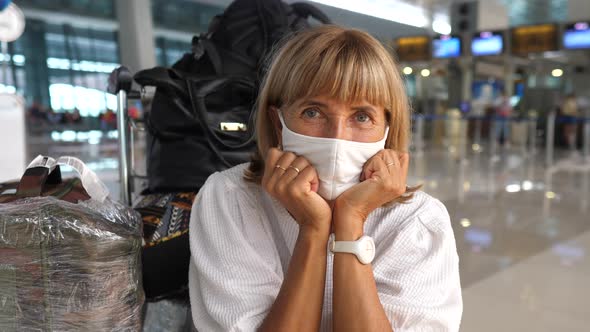 Portrait of a Tired Middle Aged Woman in a Face Mask Looking Into Camera Sitting Next to Her Luggage