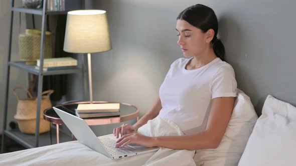 Young Latin Woman Working on Laptop in Bed 