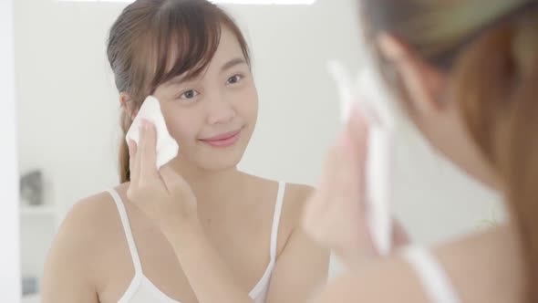 Young asian woman smile and joy with skin care use oil blotting paper on face looking mirror.