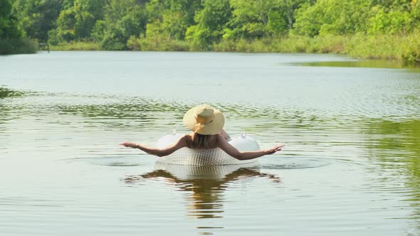 Woman in swimsuit and straw hat is floating with an inflatable circle in lake river pond
