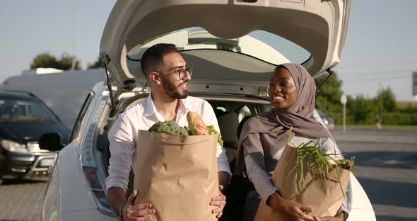 Diverse Couple with Grocery in Paper Bags at Car Trunk