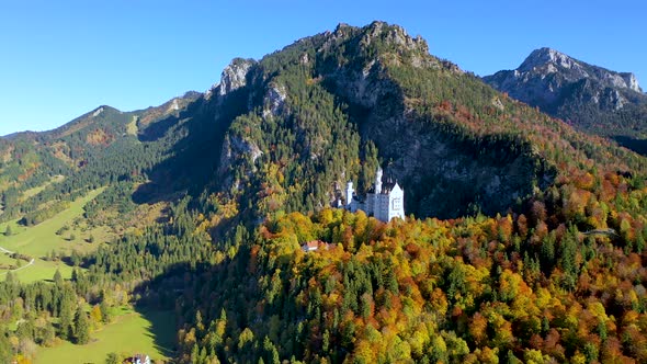 Beautiful Neuschwanstein castle on top of a Mountain with autumn color tree background, Aerial